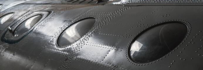A number of portholes in the body of the vehicle. Metal texture with rows of rivets. Selective...
