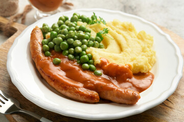 Bangers and mash. Grilled sausages with mash potato and green pea on white plate on grey background. Traditional dish of Great Britain and Ireland. BBQ beef sausages. Top view.