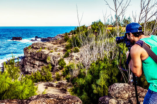 View from behind of a man standing on the shore taking pictures with a camera and tripod of the ocean and rugged coastline from Nakalele Point; Maui, Hawaii, United States of America