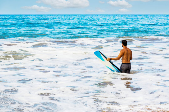 Man waiting for a sea wave while carrying a bodyboard at D. T. Fleming Beach; Kapalua, Maui, Hawaii, United States of America