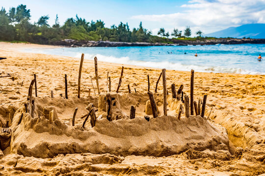 A sandcastle with sticks around the edges on the shore of D. T. Fleming Park, with swimmers in the water and the Island of Molokai in the background; Kapalua, Maui, Hawaii, United States of America