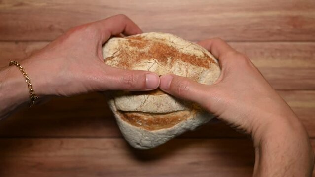 Top view of male hands trying to break some hard bread. Background of a wooden table.