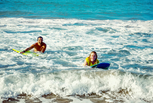 Happy married couple playing in the waves with bodyboards at D. T. Fleming Beach; Kapalua, Maui, Hawaii, United States of America