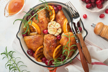 Baked chicken thighs with orange, cranberry and spicy herbs rosemary servered in frying pan on light background. Festive Christmas Dinner Concept menu. Top view. copy space
