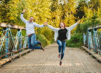 Mature married couple outside in a park leaps in mid-air in exuberant celebration; Edmonton, Alberta, Canada
