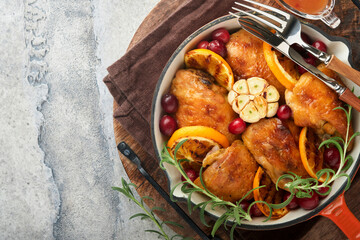 Baked chicken thighs with orange, cranberry and spicy herbs rosemary servered in frying pan on light background. Festive Christmas Dinner Concept menu. Top view. copy space
