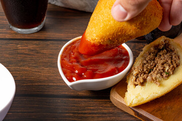 dipping coxinha on the ketchup sauce. traditional brazilian fried coxinha snack fast food
