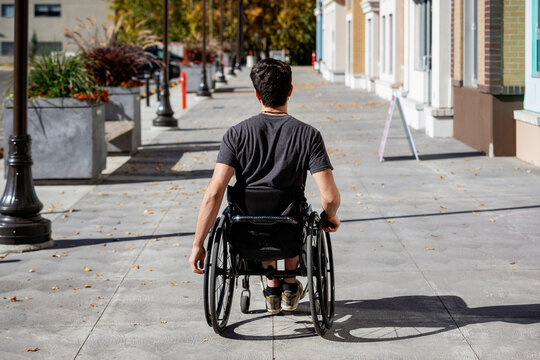 Young paraplegic man in his wheelchair going down a city walkway on a beautiful fall day; Edmonton, Alberta, Canada