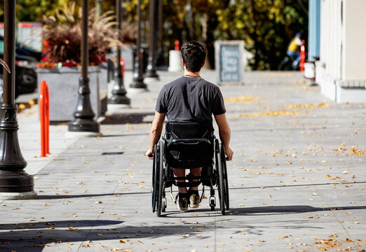Young paraplegic man in his wheelchair going down a city walkway on a beautiful fall day; Edmonton, Alberta, Canada