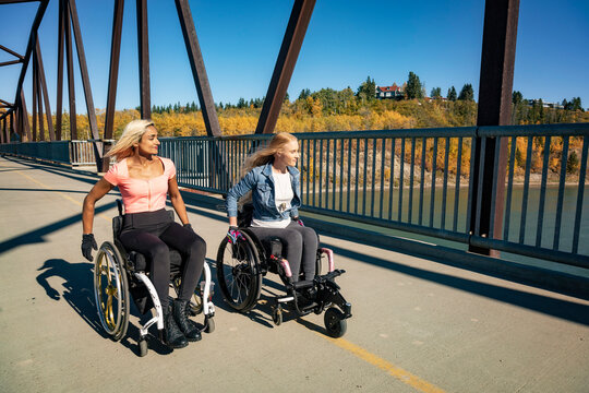 Two young paraplegic women in their wheelchairs in a park on a beautiful fall day; Edmonton, Alberta, Canada