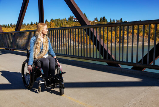 Young paraplegic woman going across a bridge using her wheelchair on a beautiful fall day; Edmonton, Alberta, Canada