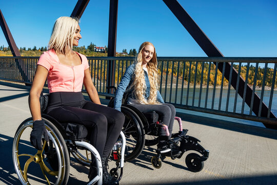 Two young paraplegic women in their wheelchairs in a park on a beautiful fall day; Edmonton, Alberta, Canada
