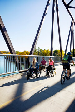 Three young paraplegic friends spending time together moving across a park bridge in their wheelchairs in a city park on a beautiful day; Edmonton, Alberta, Canada