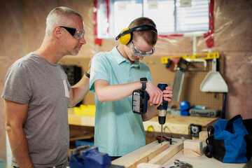 Young man doing woodworking in his basement while his father looks on; Edmonton, Alberta, Canada