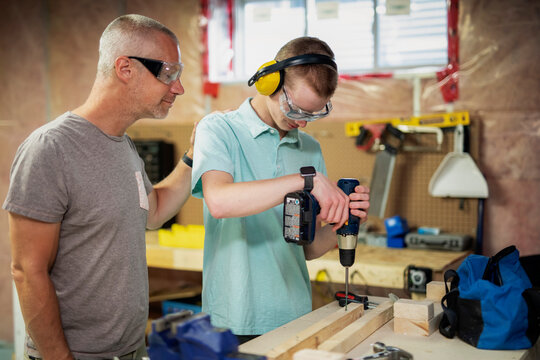 Young man doing woodworking in his basement while his father looks on; Edmonton, Alberta, Canada