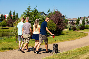 Family with two teenage sons walk together in a neighbourhood park with their dog on a beautiful sunny day; Edmonton, Alberta, Canada