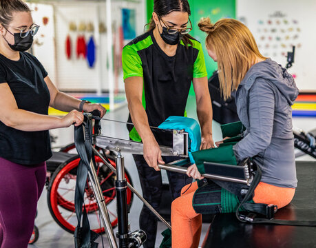 A paraplegic woman working out using an assisted walking machine with her trainers; Edmonton, Alberta, Canada
