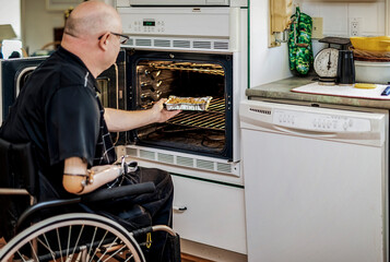 Man with double limb amputations using the oven in the kitchen at home; St. Albert, Alberta, Canada