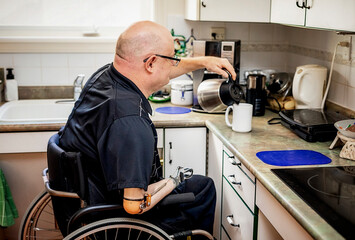 Man with double limb amputations pouring coffee in the kitchen at home; St. Albert, Alberta, Canada