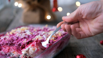 Homemade New Year is a herring salad under a fur coat on a wooden background. A man's hand lays a...