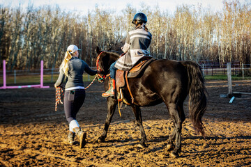A trainer working with a young girl with Cerebral Palsy during a Hippotherapy session; Westlock, Alberta, Canada