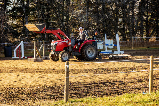 A woman grooming a corral in preparation for horse training sessions using a corral rake; Westlock, Alberta, Canada