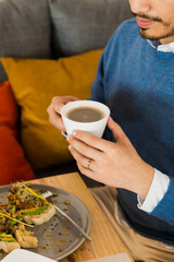 Hands of an unrecognizable person holding a cup of coffee, wearing formal wear.