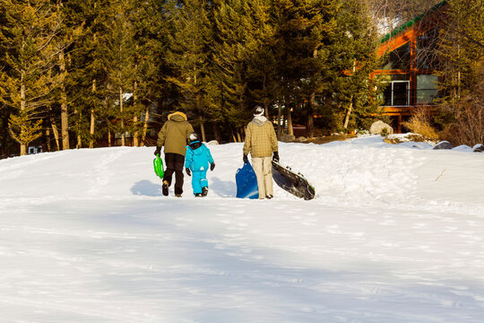Two Men Walking With A Child After Sledding In A Mountain Resort; Fairmont Hot Springs, British Columbia, Canada
