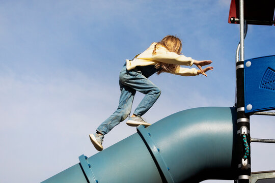 Young girl running on the top as she climbs up a tube slide in a school playground on a warm fall afternoon; St. Albert, Alberta, Canada