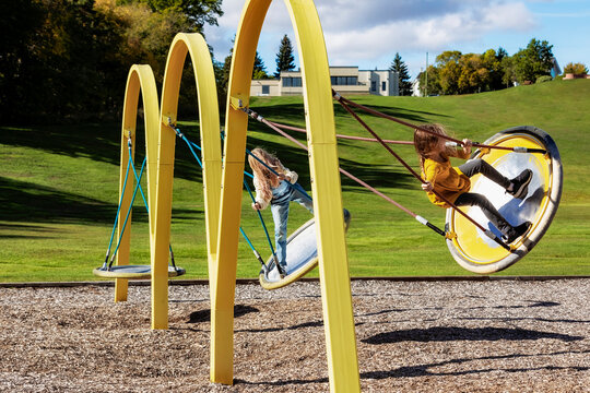 Young girls swinging on saucer swings in a playground on a warm fall afternoon; St. Albert, Alberta, Canada