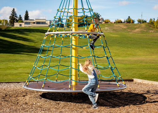 Two sisters playing on a merry-go-round in a school playground on a warm fall afternoon; St. Albert, Alberta, Canada
