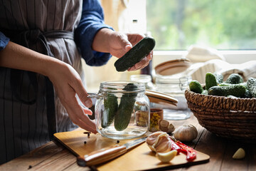 Fototapeta na wymiar Woman putting cucumbers into jar at wooden table, closeup. Pickling vegetables