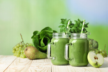 Mason jars of fresh green smoothie and ingredients on wooden table. Space for text