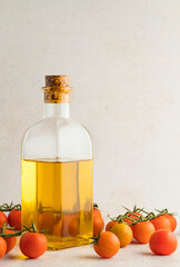 Glass bottle with extra virgin olive oil with some colorful cherry tomatoes on a light stone background.