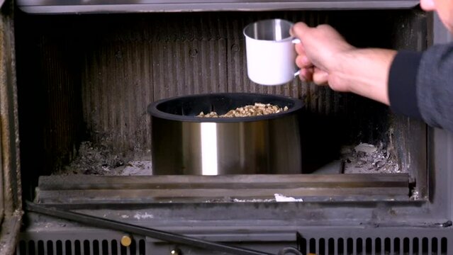 A man loads pellets into the fireplace with a white mug. High quality 4k footage