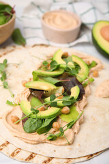 Tortilla with hummus and vegetables on table, closeup