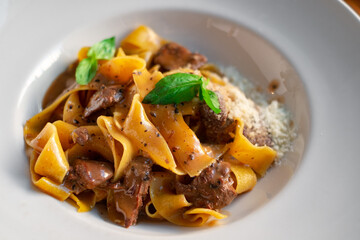 Papardelle pasta with beef, gravy, parmesan and basil on a white plate. Italian dish served