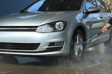 Man washing auto with high pressure water jet at outdoor car wash, closeup