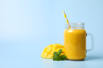 Mason jar with delicious fruit smoothie and fresh mango on light blue background. Space for text