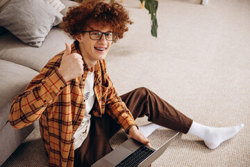Young man working on laptop at home sitting bu the sofa