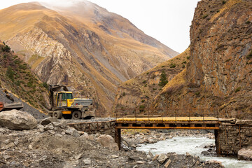 The excavator restoring the road destroyed by the mudflow. Road machinery on the bridge and beautiful mountains in the background. Oysor river, Chirkhalyu or Chvakhilo waterfall in Dagestan, Russia.