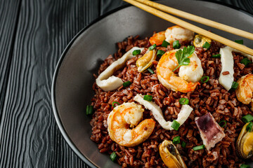delicious red rice with shrimps and seafood on a black wooden rustic background