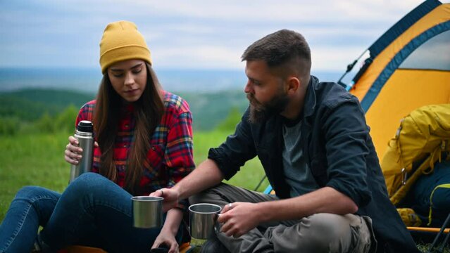 Couple of campers drinking coffee from metal cups and a thermos while in nature