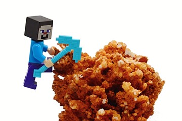 Fototapeta premium LEGO Minecraft figure of Steve with diamond pickaxe trying to mine real orange Calcite mineral, polymorph of Calcium Carbonate, white background