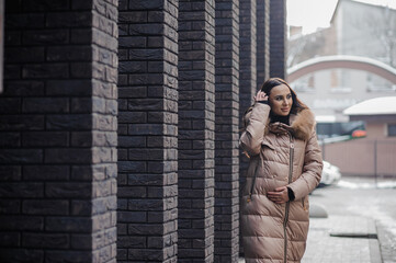 Beautiful young pregnant woman in a brown coat, in the background a brick wall