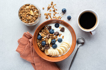 Yogurt with granola, banana, blueberries and dark chocolate chunks in a bowl served with cup of...