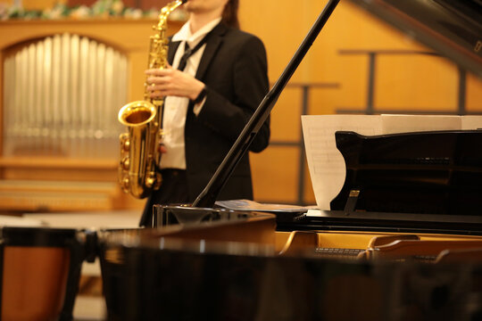 Background musical image with an open grand piano and a musician in a black suit playing the saxophone