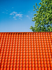 Red tiled roof. CLouds in blue sky. Green tree. Spring or summer nature.
