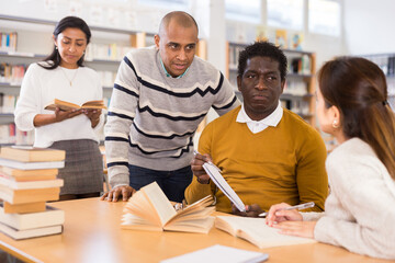 Group of friendly adults people studying together in university library, reading and discussing with interest....