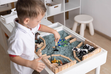Cute baby boy playing sensory box kinetic sand table with farm animals